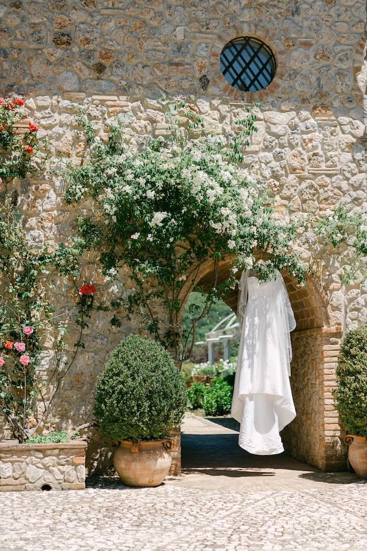 Wedding dress hanging from a flowered stone archway at an Italian country estate