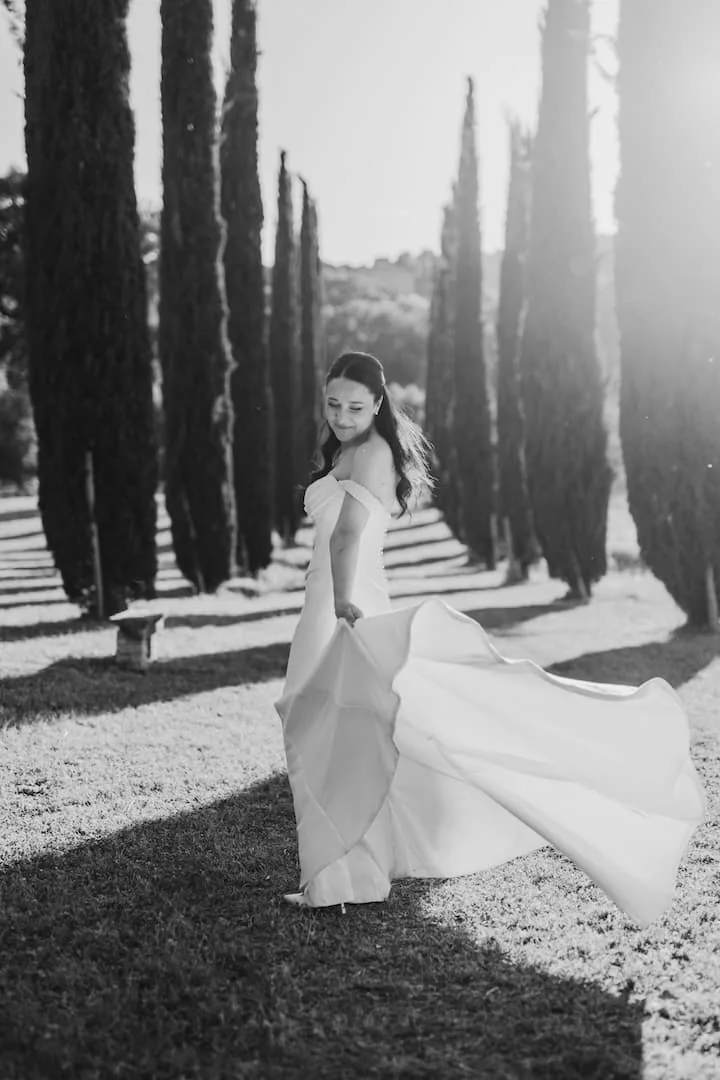 Bride swirling her dress in a cypress-lined avenue, black and white wedding photograph in Tuscany