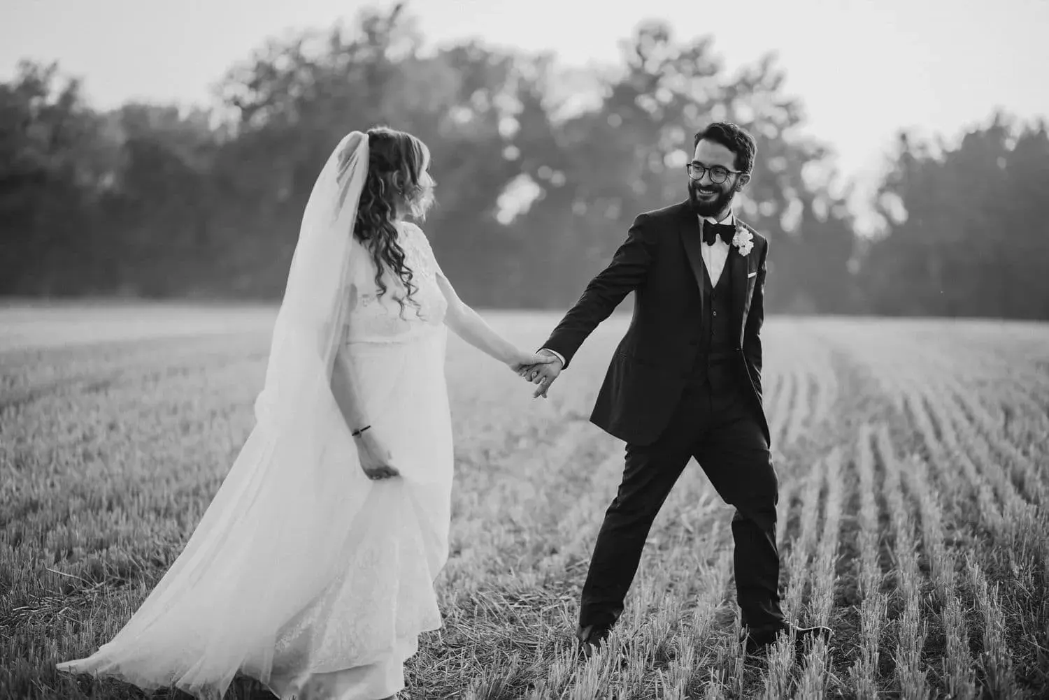 Gli sposi mano nella mano nel campo, in bianco e nero