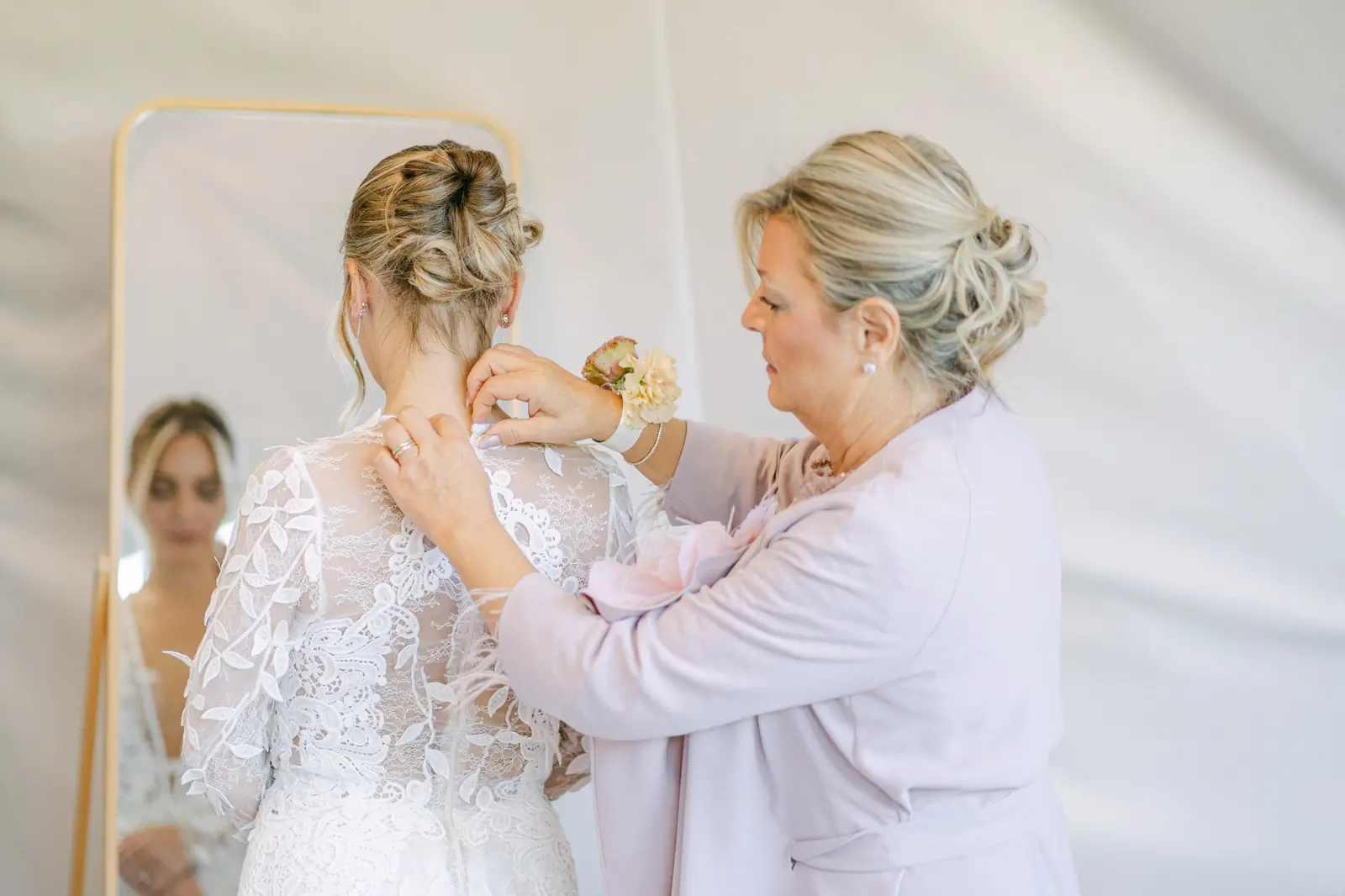 The bride being helped into her dress in front of the mirror