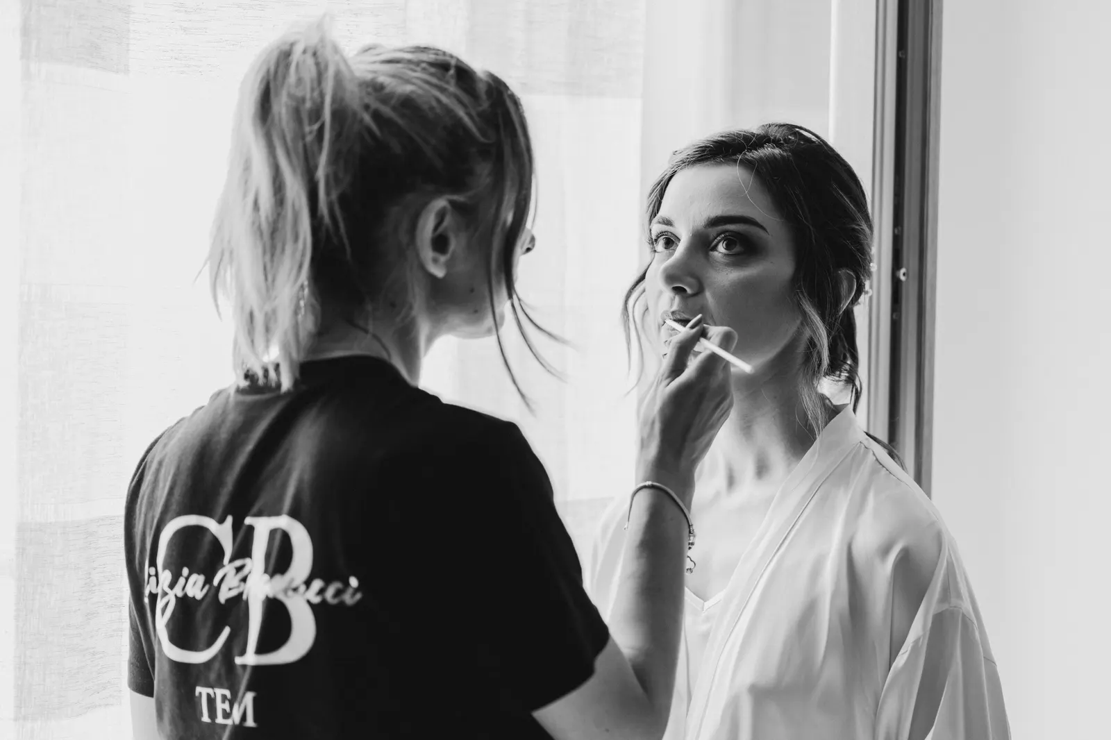The bride's make-up being done by the window, in black and white