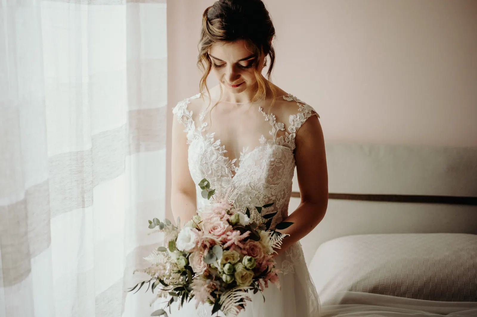 The bride looking at her bouquet by the window, in the natural light of the room