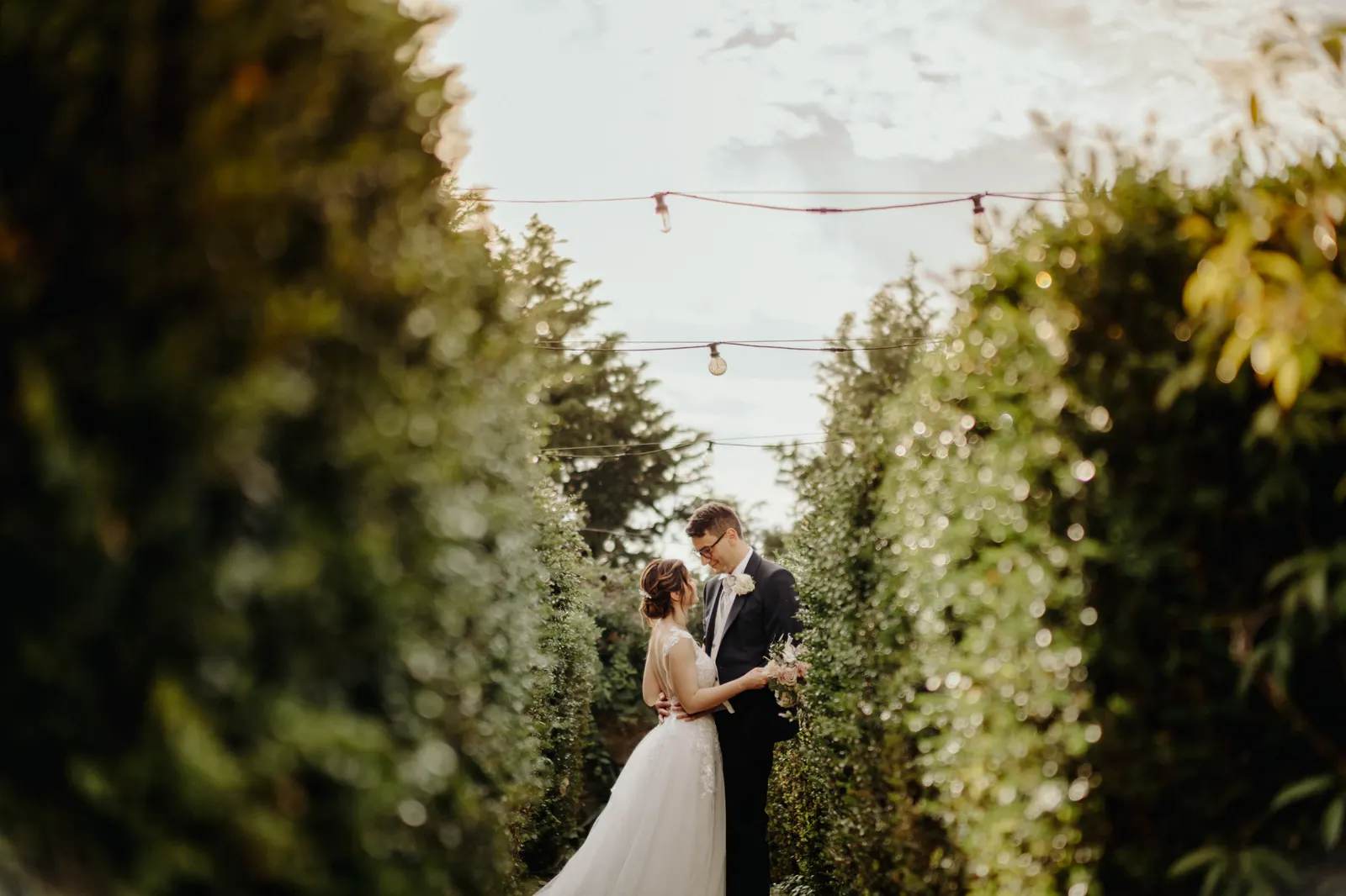 Martina and Daniele in the hedge avenue under the string lights, in low sun