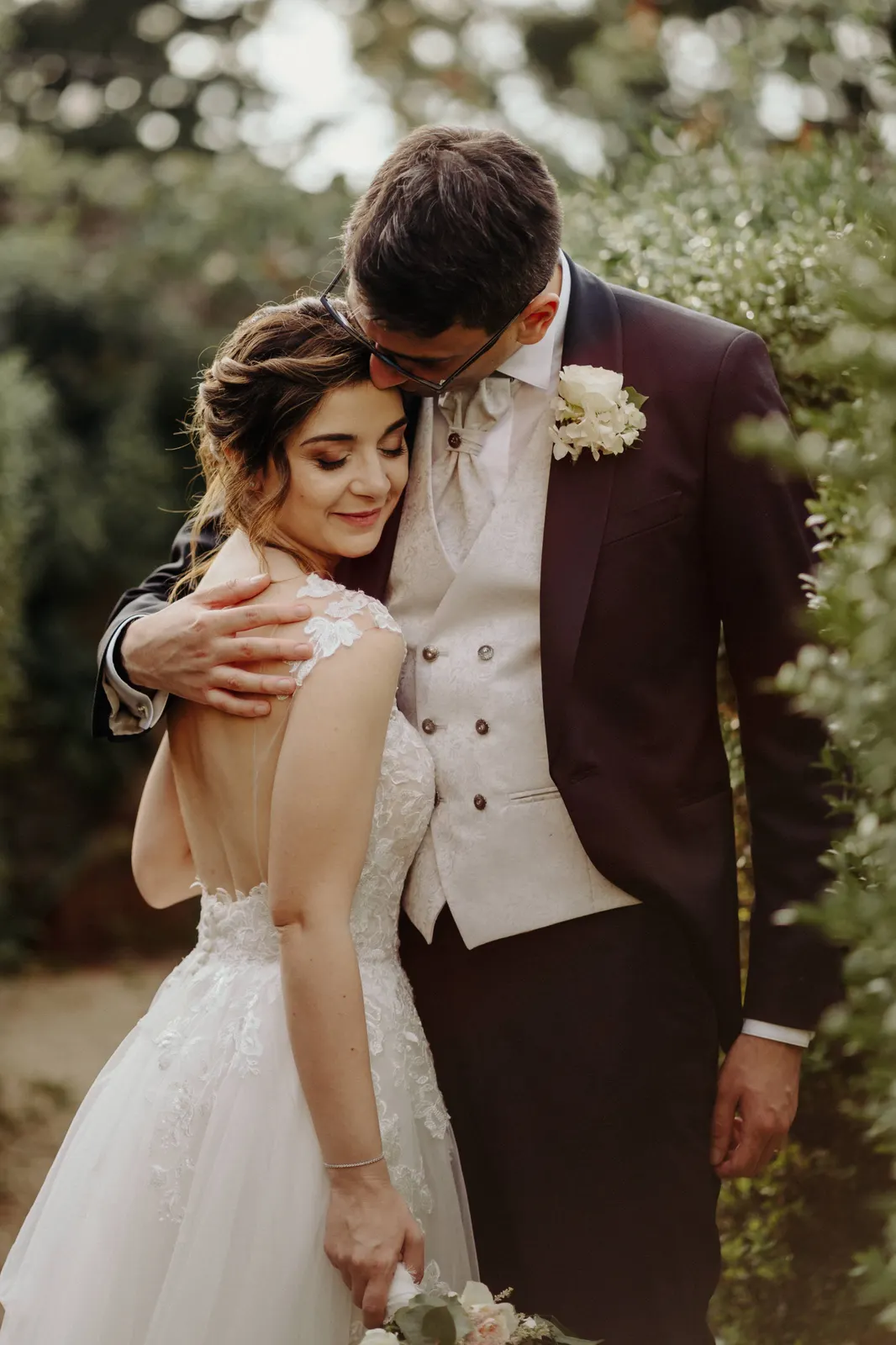 Daniele kissing Martina's forehead as they embrace among the hedges