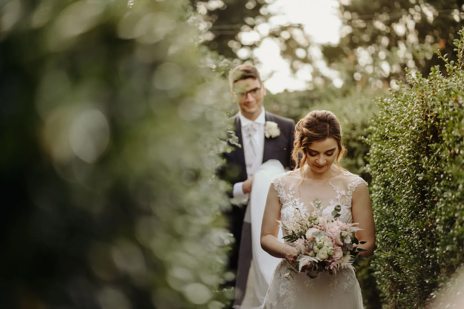 The couple walking among the castle hedges, the bride holding her bouquet