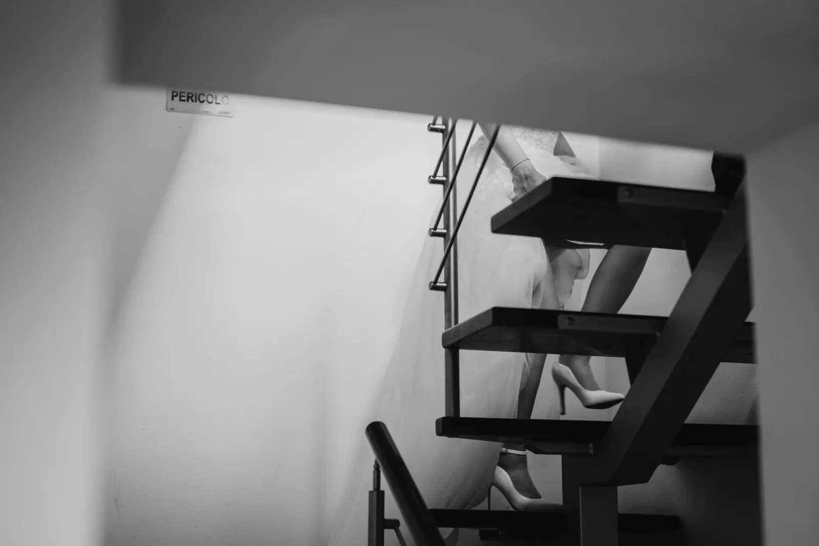 The bride coming down an indoor staircase, her shoes and train in view, in black and white