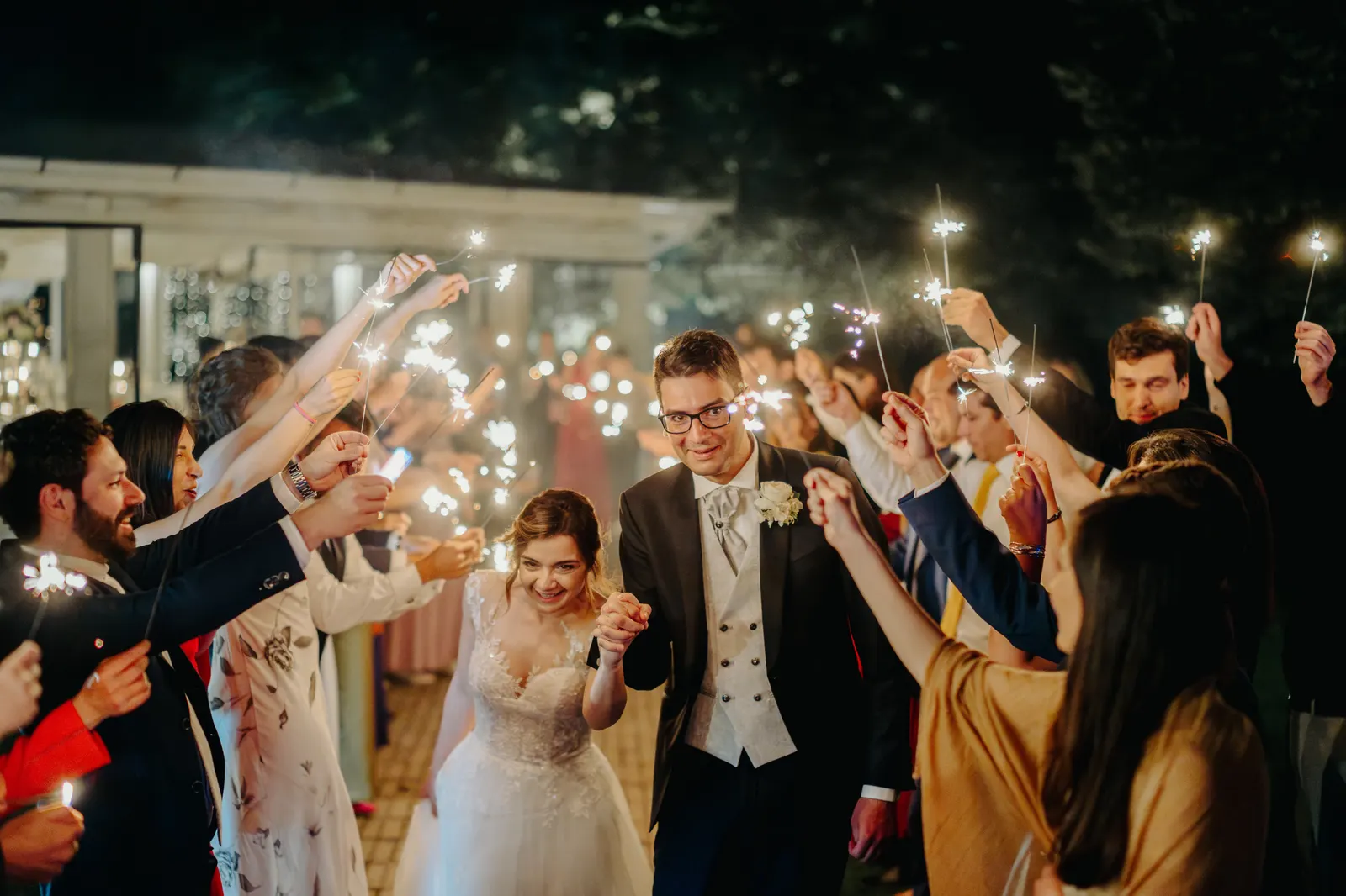 The couple among guests holding up sparklers in the evening