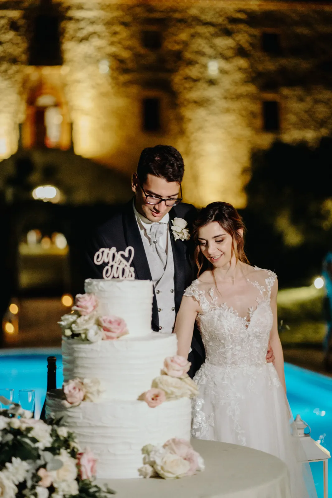 Cutting the cake by the pool, with Castello di Montignano lit up behind