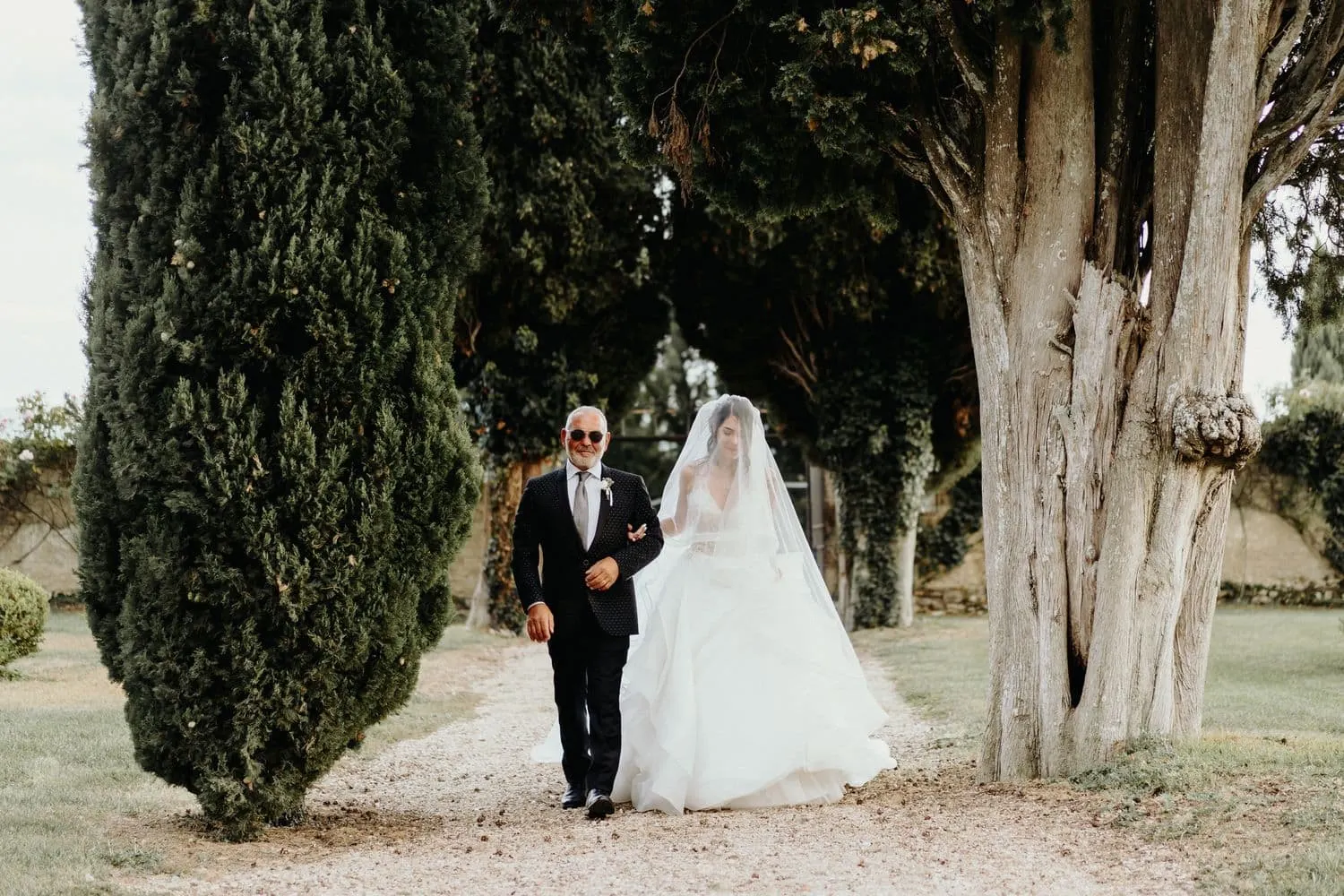 Micaela percorre il viale dei cipressi al braccio del padre