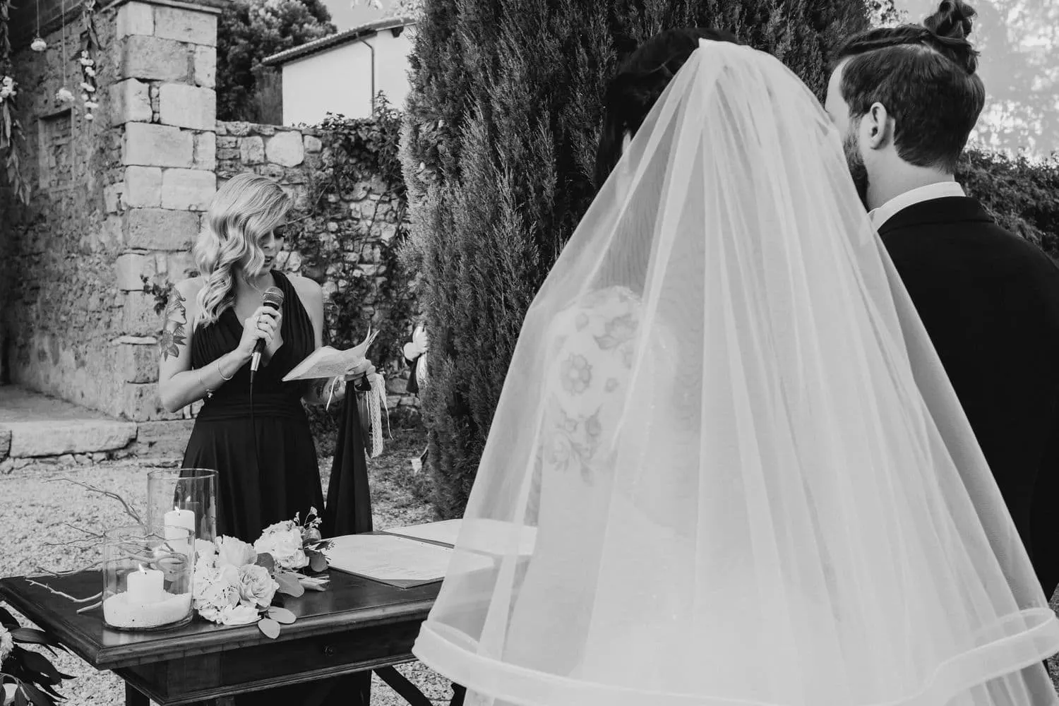 Un'amica legge al microfono, con il velo della sposa in primo piano, in bianco e nero