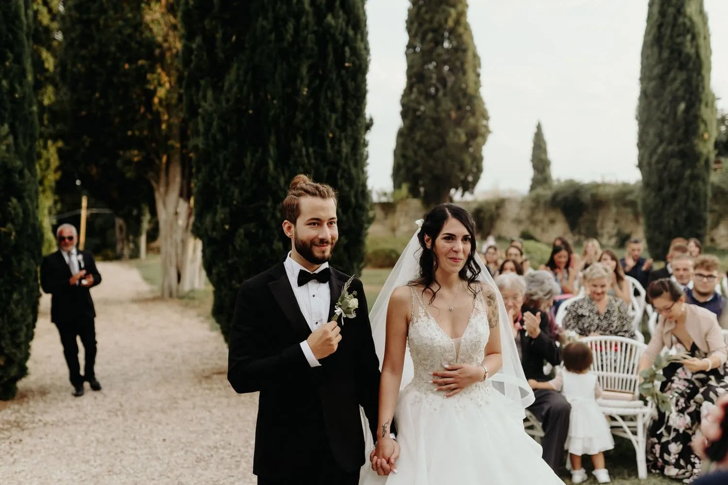 Gli sposi in piedi davanti agli invitati lungo il viale