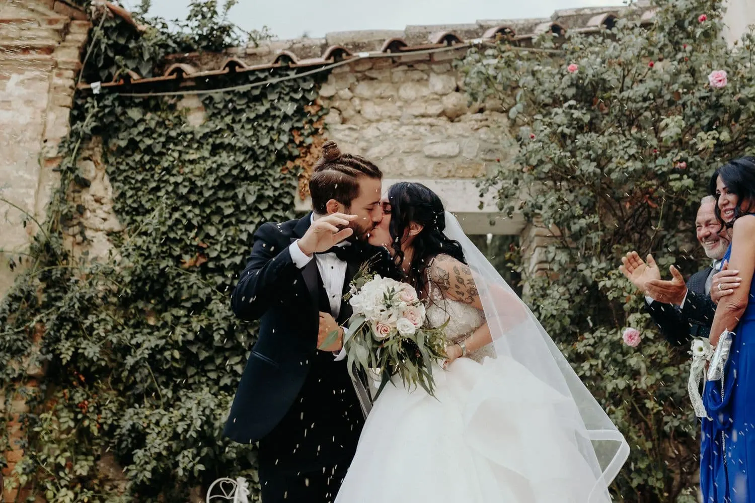 Il bacio degli sposi sotto i petali, davanti al muro d'edera