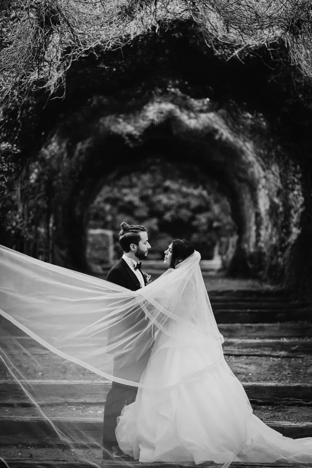 Micaela's long veil stretched out in the wind under the tunnel of trees, in black and white