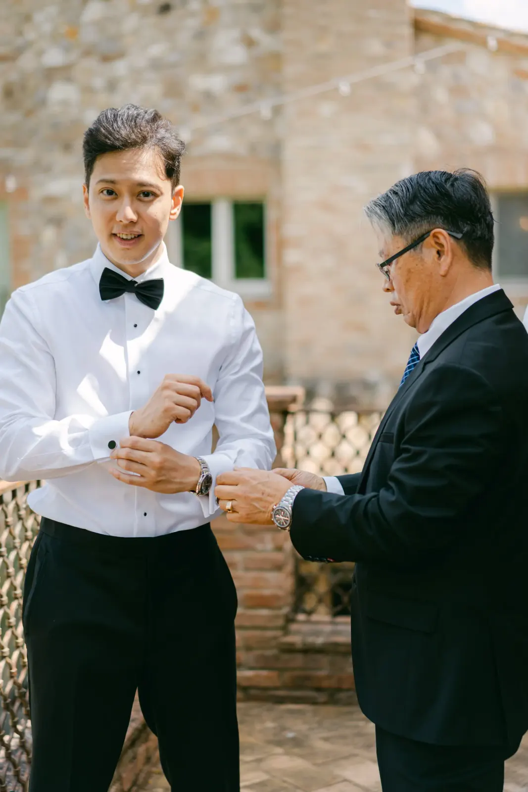 James fastening his shirt cuffs beside his father in the stone courtyard