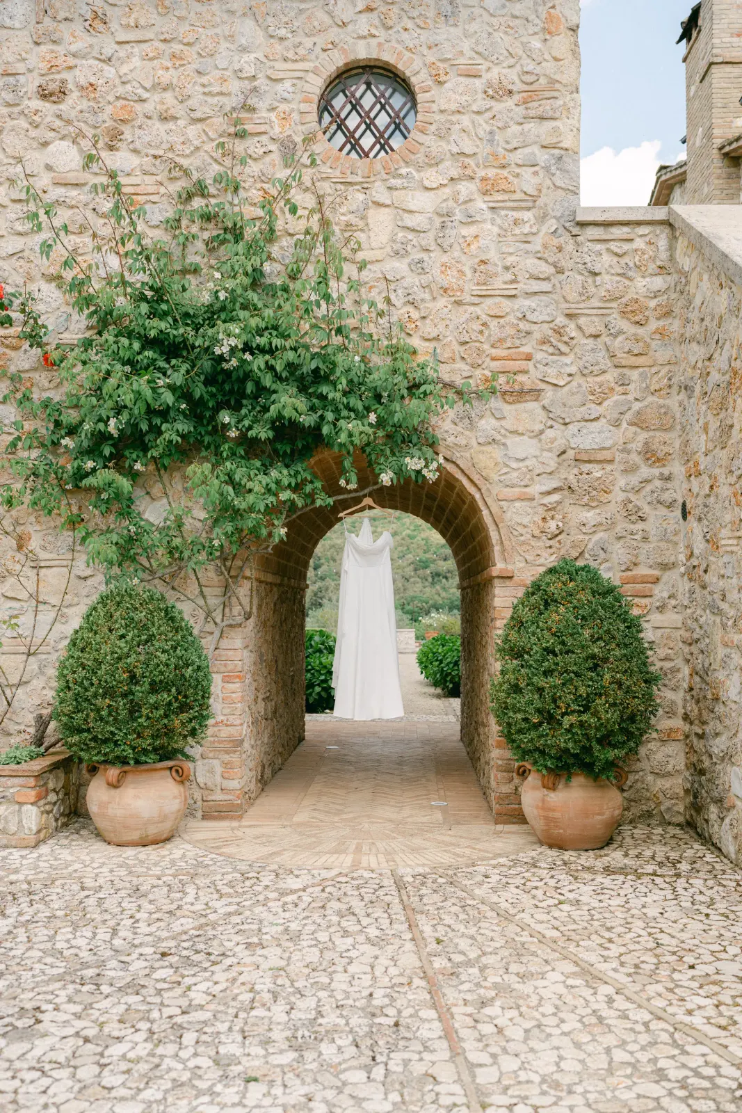The wedding dress hanging under a stone archway, with the garden of Tenuta del Gallo behind