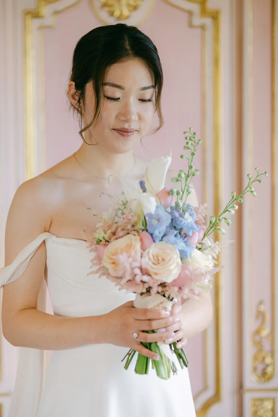 Audrey looking at her blue and peach bouquet in a room with pink and gold walls