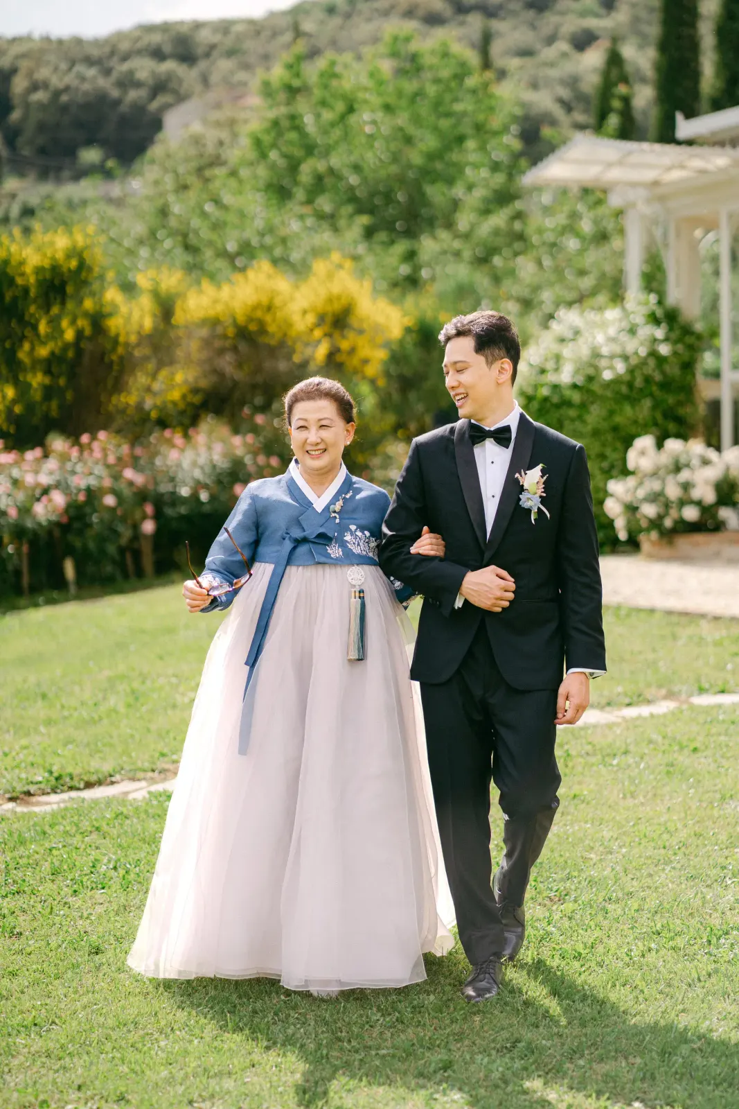 James's mother in a hanbok walking her son across the lawn
