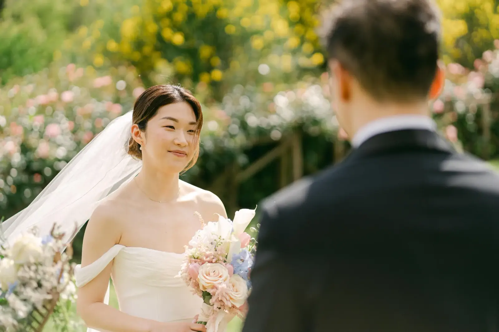 Audrey smiling at James during the ceremony, among the garden flowers