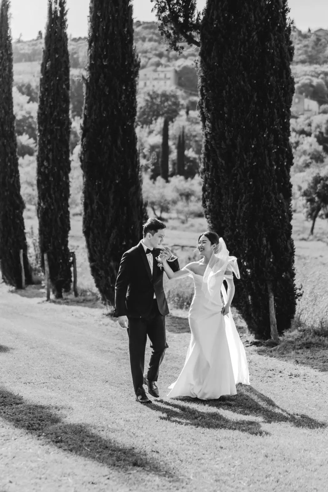 Audrey and James laughing as they walk among the cypresses, in black and white