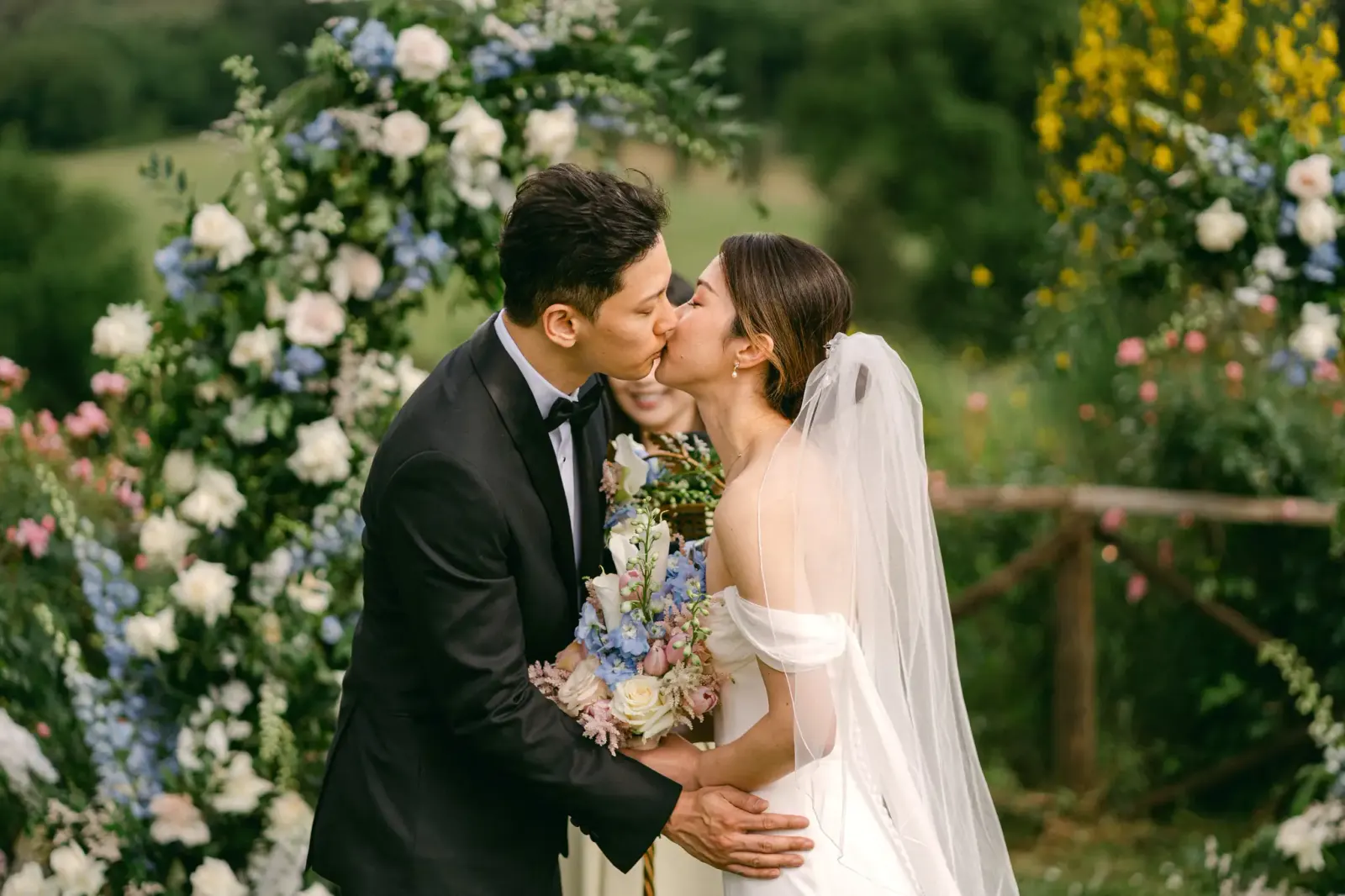 The couple's kiss in front of the arch of blue and white flowers