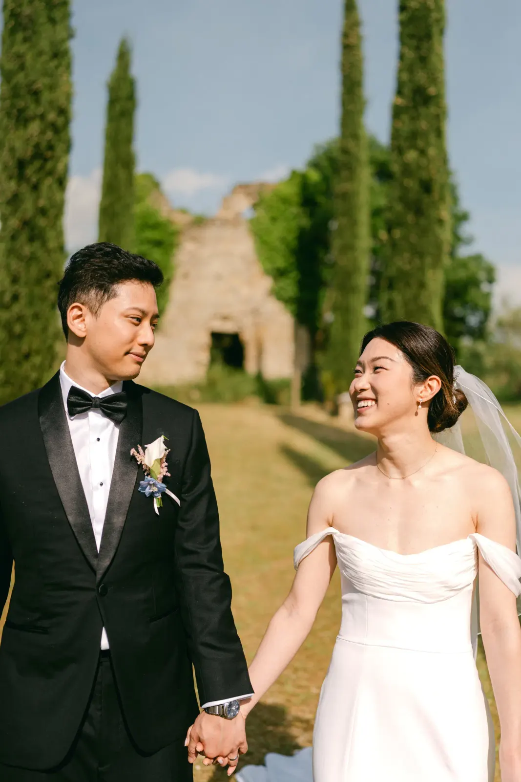The couple hand in hand, smiling at each other, with the cypresses behind