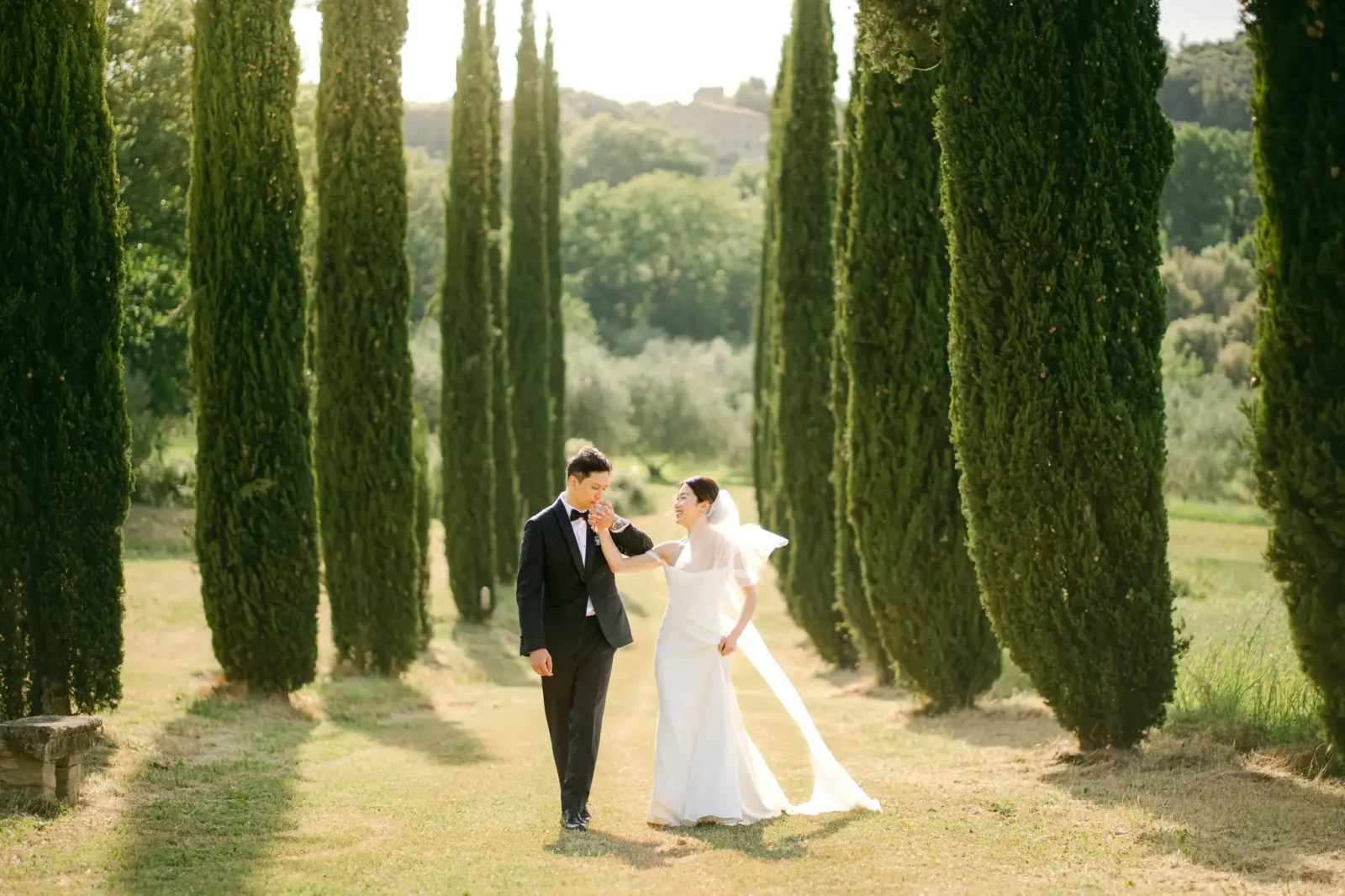 Audrey and James strolling among the cypresses, her long veil brushing the grass