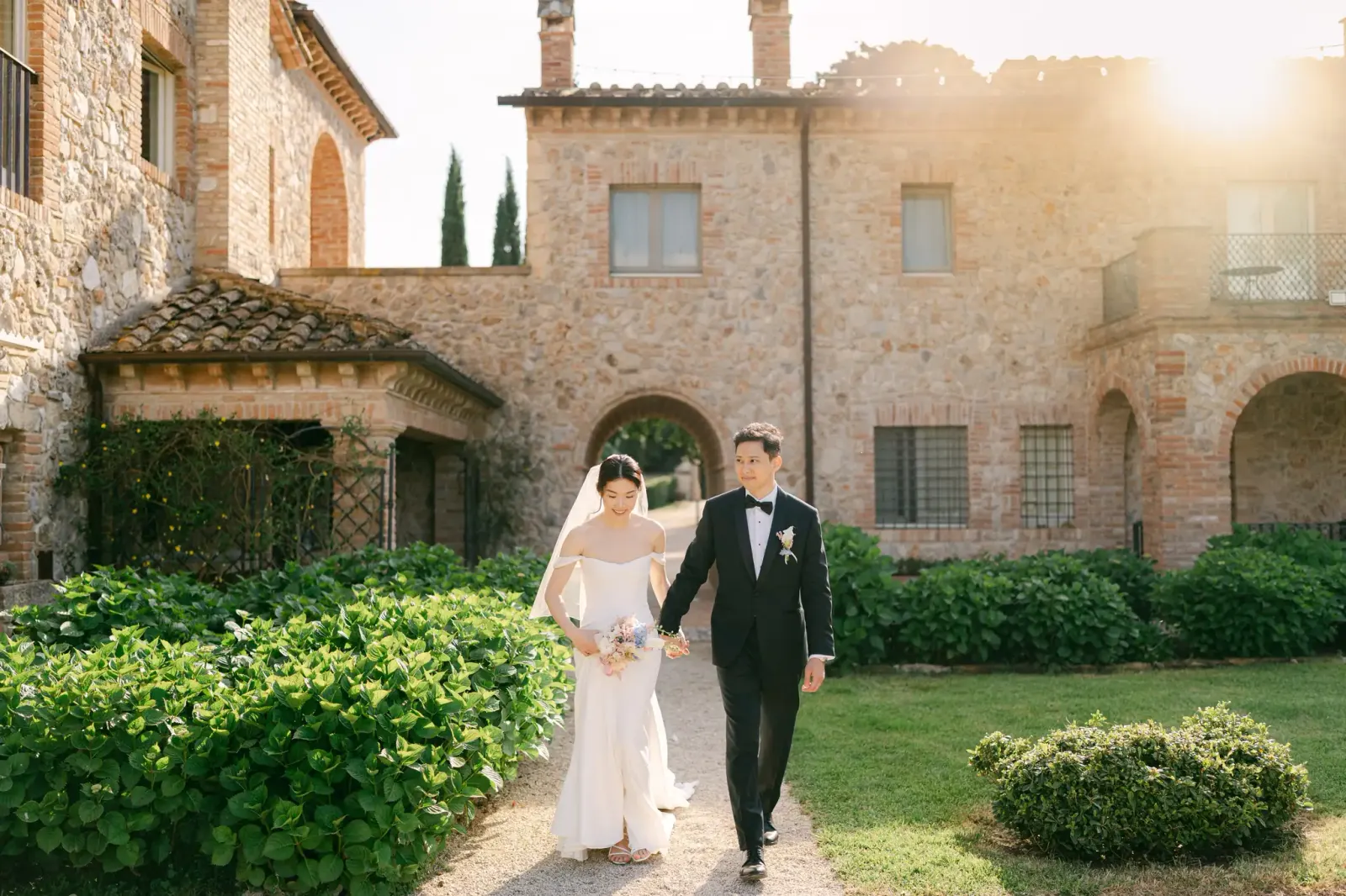 Audrey and James walking in the garden with the stone villa behind them, at sunset