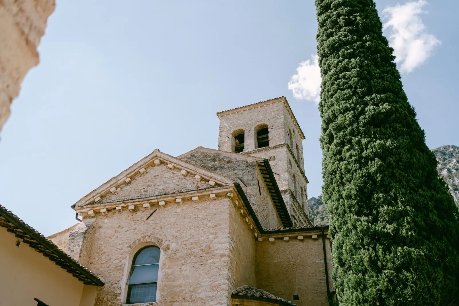 La chiesa e il campanile dell'Abbazia San Pietro in Valle accanto a un cipresso