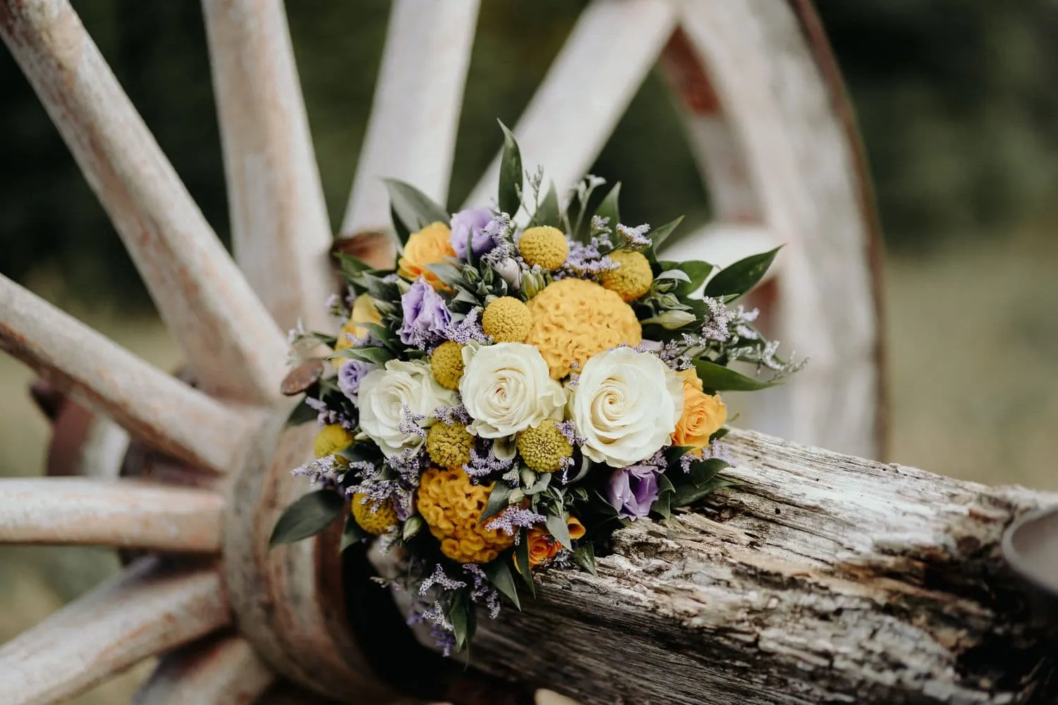 The bouquet of yellow, white and lilac flowers resting on a wooden cartwheel
