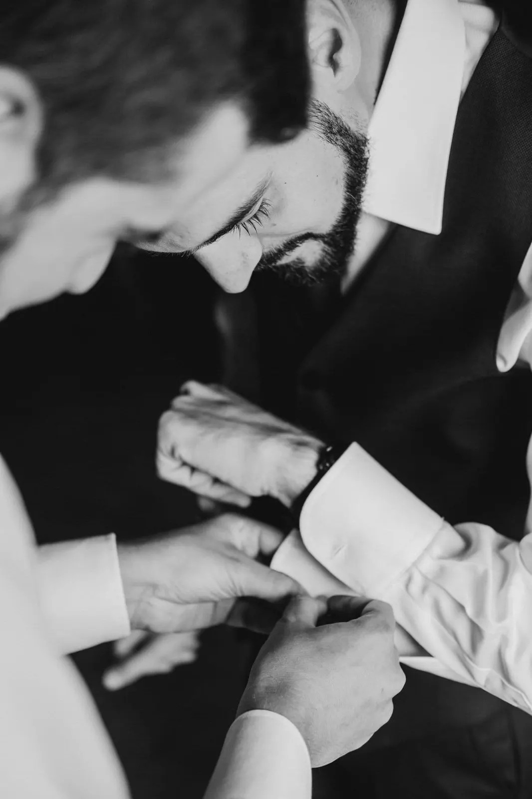 The groom being helped with his cufflinks, in black and white