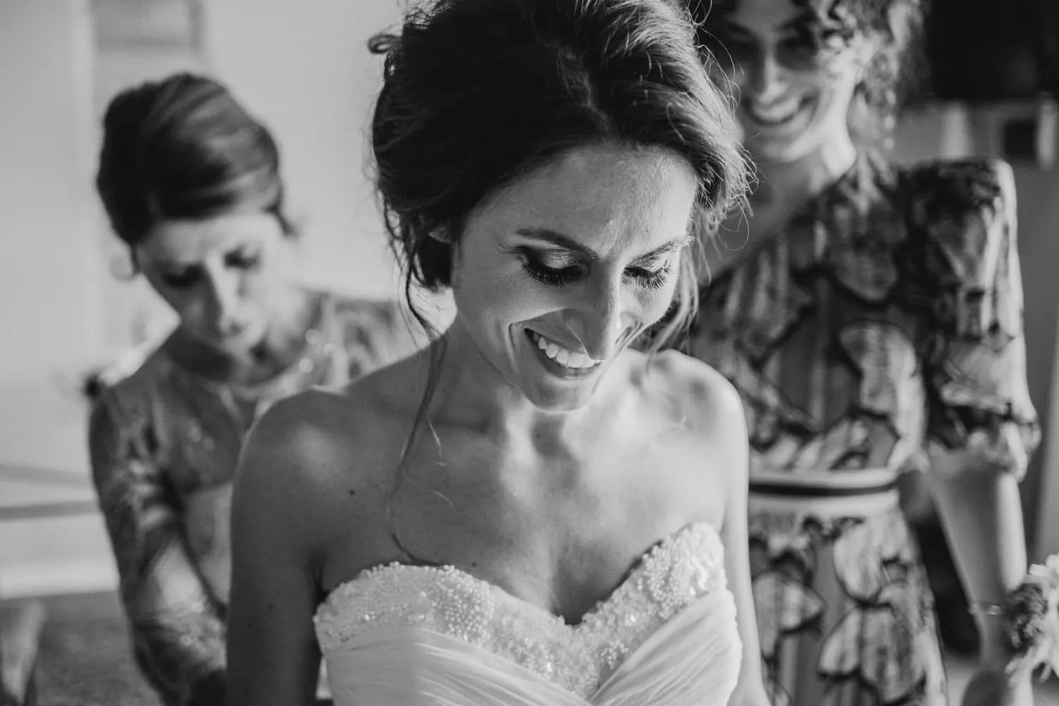 The bride's smile as her dress is fastened, in black and white