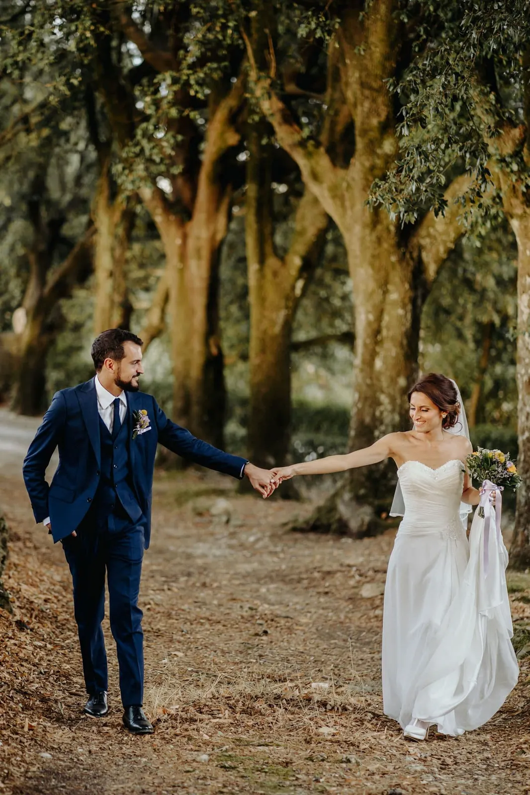 The couple hand in hand among the tall trunks of the woods