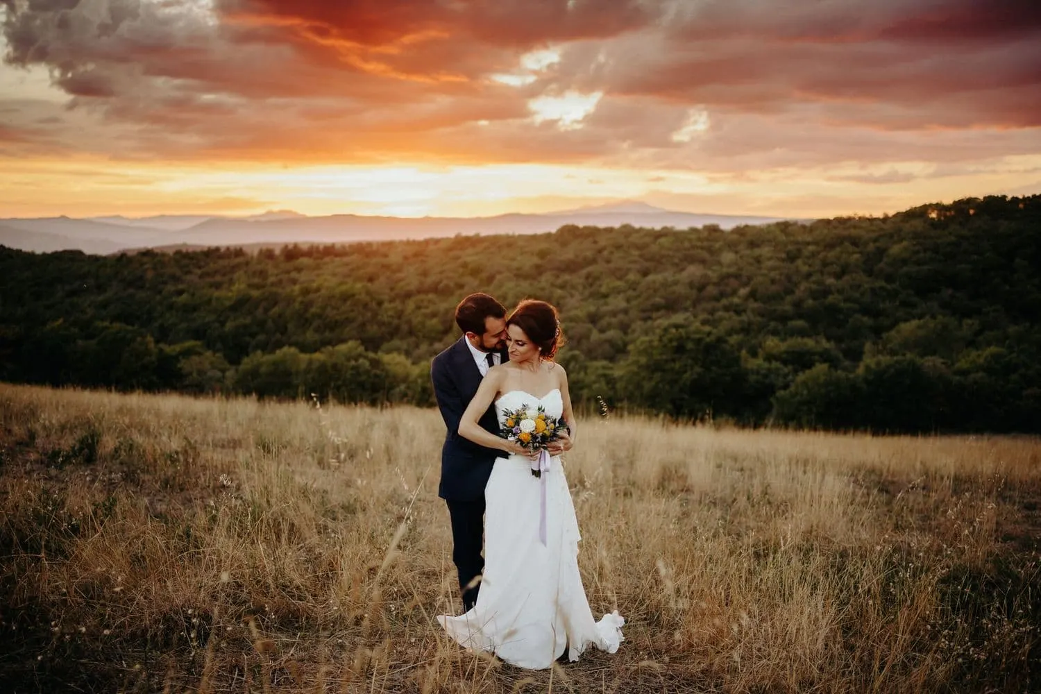 The couple embracing in the field, under the red sunset sky
