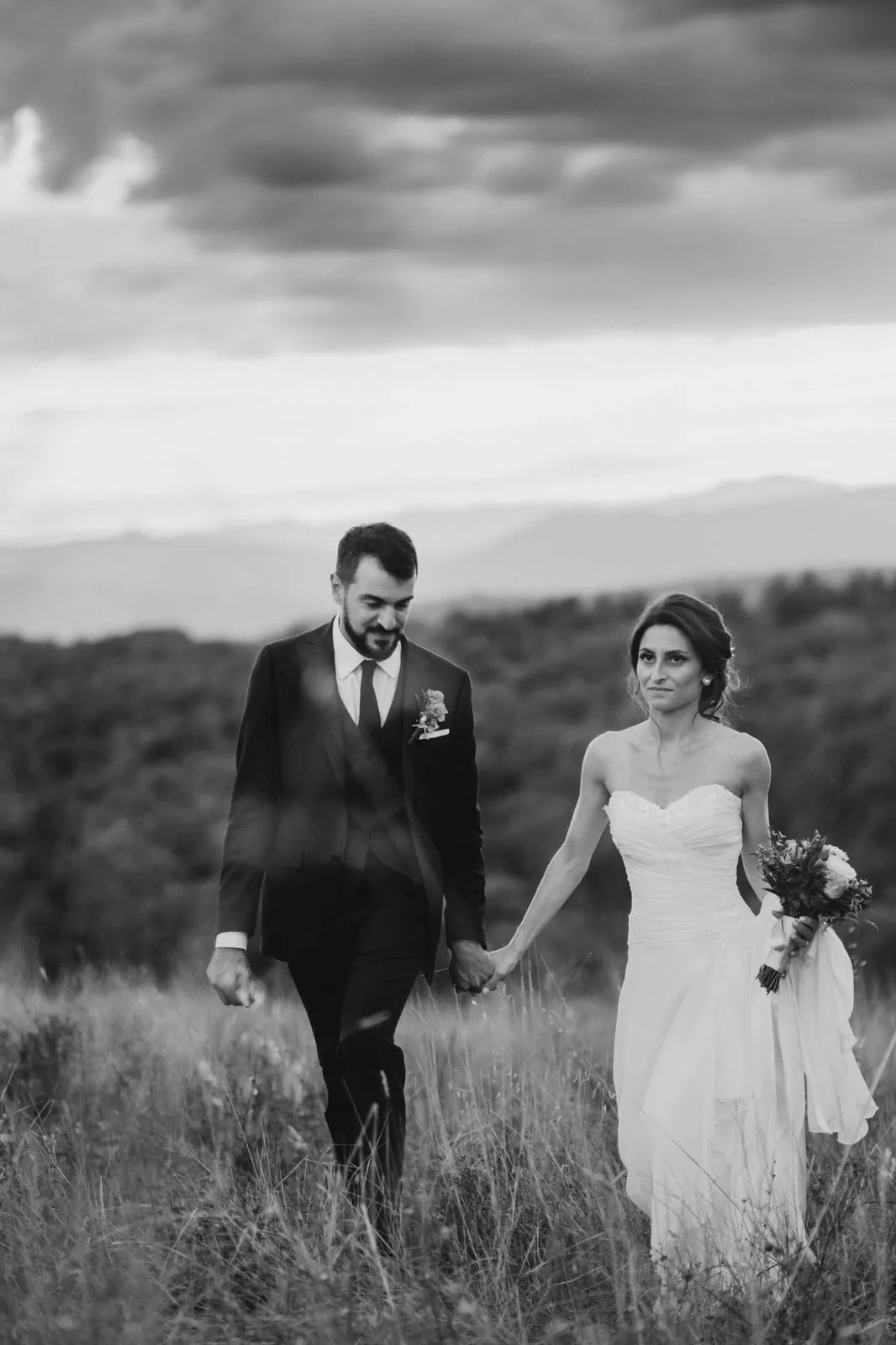 The couple walking hand in hand through tall grass, in black and white