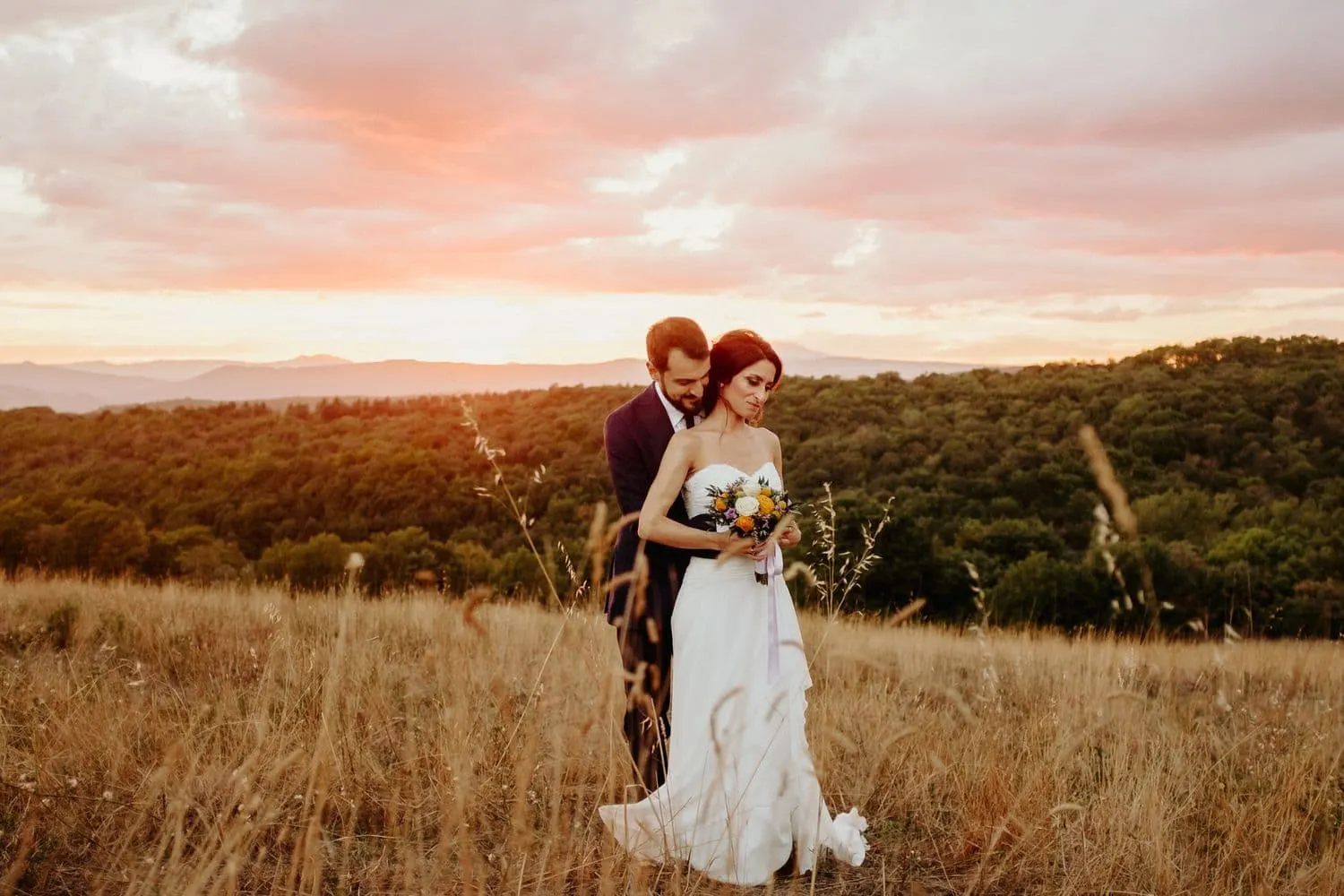 The couple embracing in the field under a pink sky